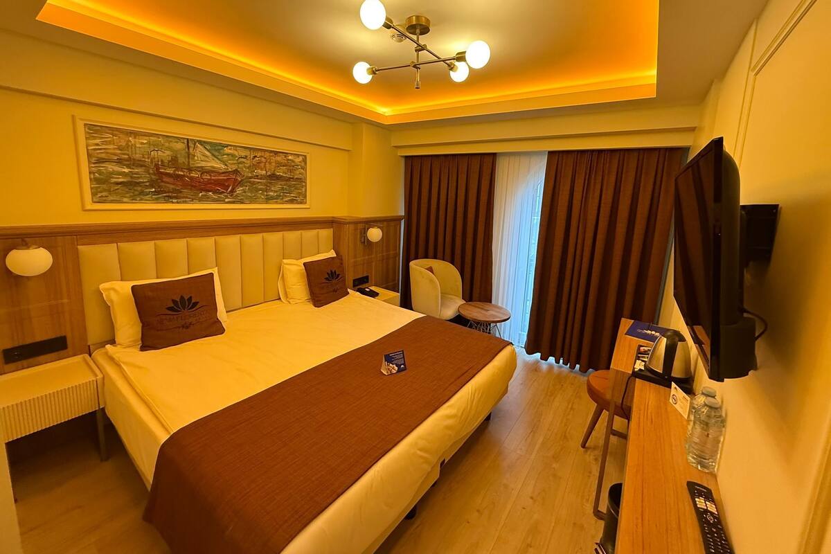 Una habitación de hotel con una cama grande, un escritorio con silla, una televisión y un cuadro en la pared.