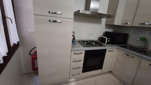 A compact kitchen with white cabinets, a gas stove, a microwave, and a stainless steel range hood. - Sweet Venice - rooms & apartments (Venice)