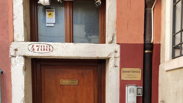 A wooden door with a brass plate, a security camera, and a sign indicating 'Sweet Venice' with a check-in number. - Sweet Venice - rooms & apartments (Venice)