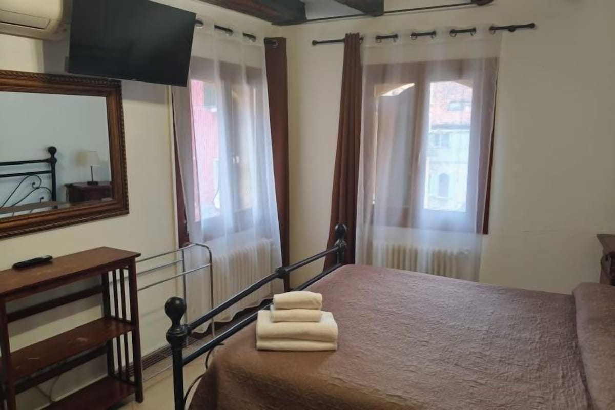A bedroom with a bed, a bedside table, a television, and curtains.