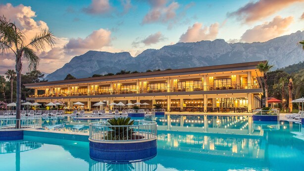 A hotel with a large pool, outdoor seating, and mountain views. - Kimeros Park Holiday Village (Kemer)
