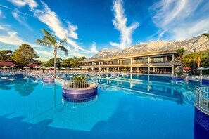 A resort pool with a view of mountains, lounge chairs, and a building with balconies.