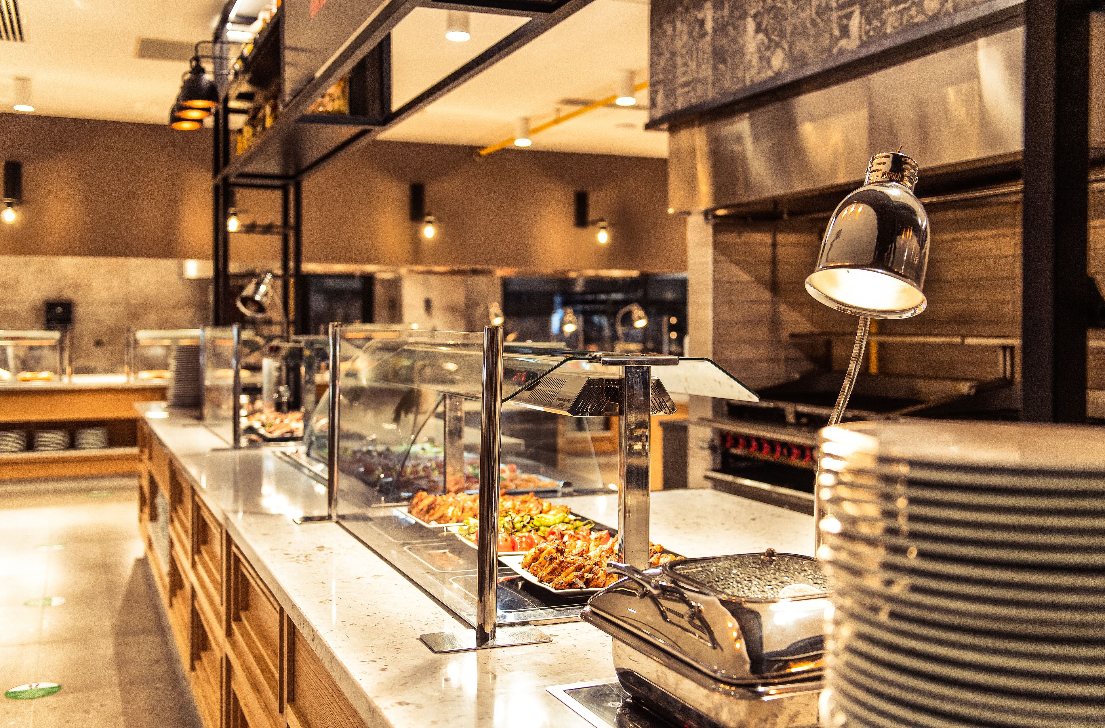 A buffet area with multiple food stations, a glass display case, and a stack of plates.