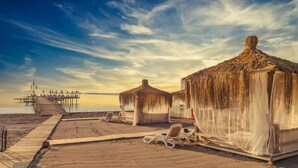 A beachside resort with thatched-roof huts, sun loungers, and a wooden pier extending into the water. - Kimeros Park Holiday Village (Kemer)