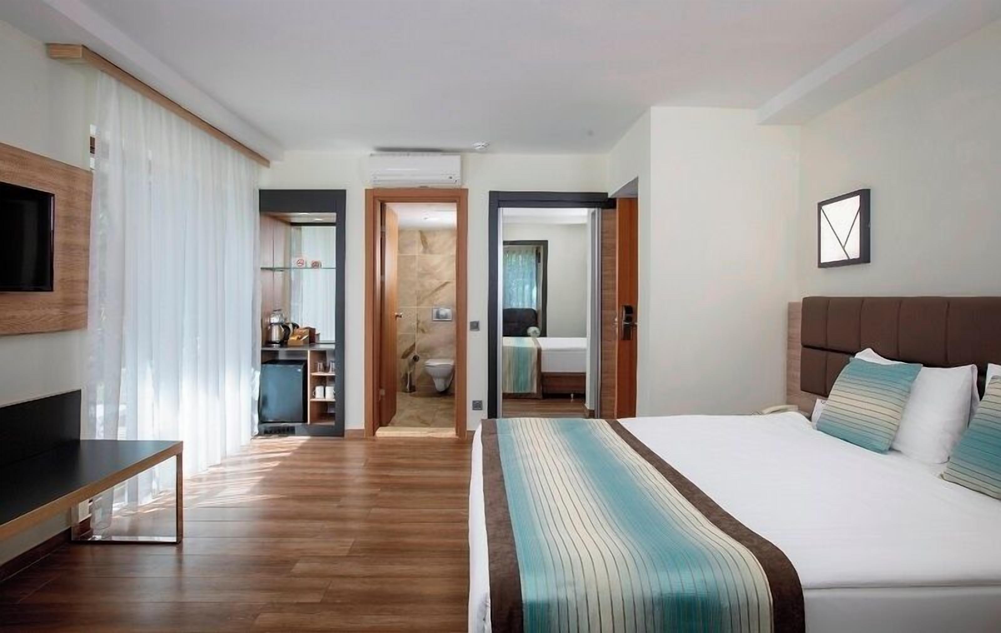 Habitació d'hotel amb un llit, televisió, escriptori i un bany visible a través d'una porta oberta.