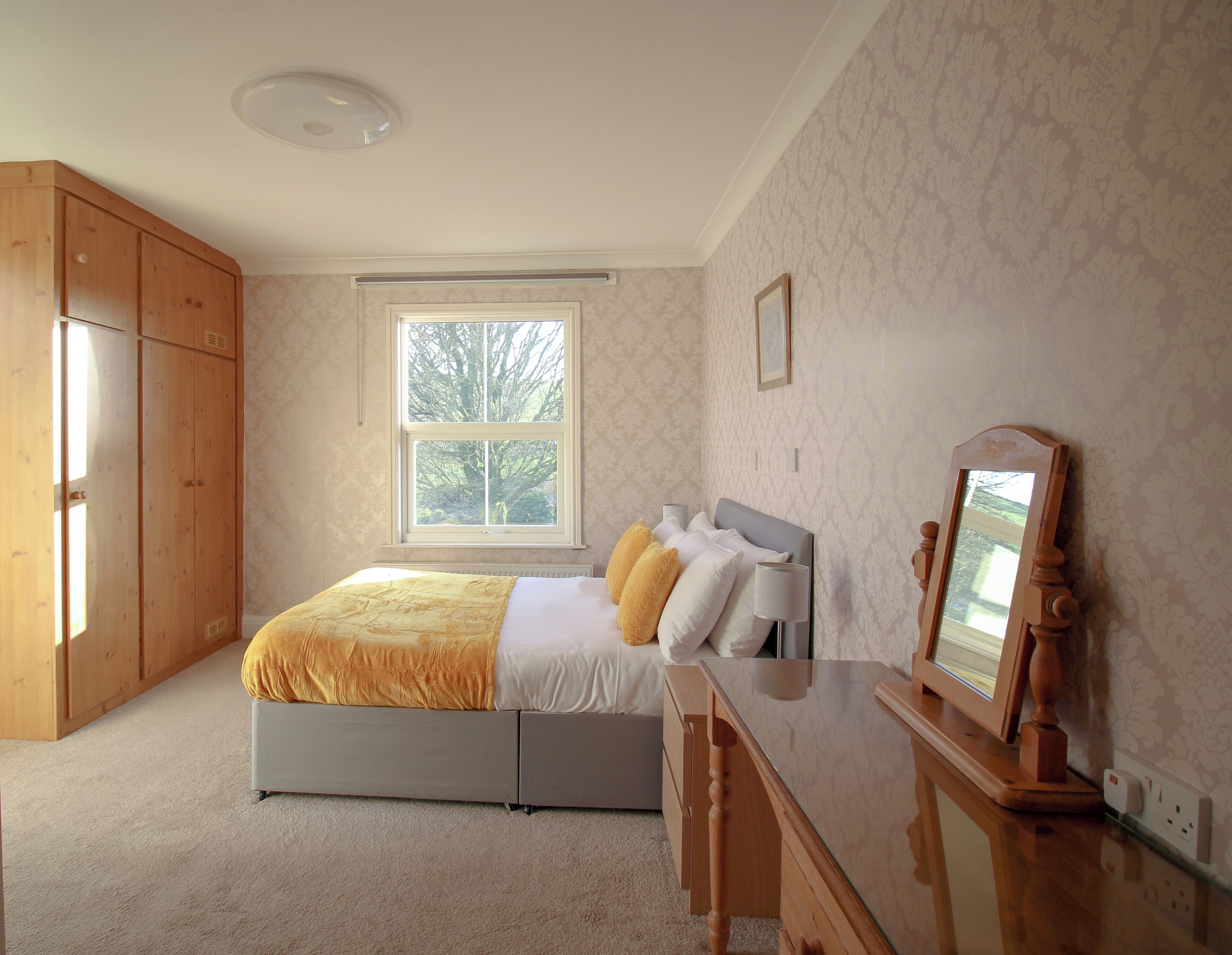 A bedroom with a bed, a dresser, a mirror, and a window with a view of trees.
