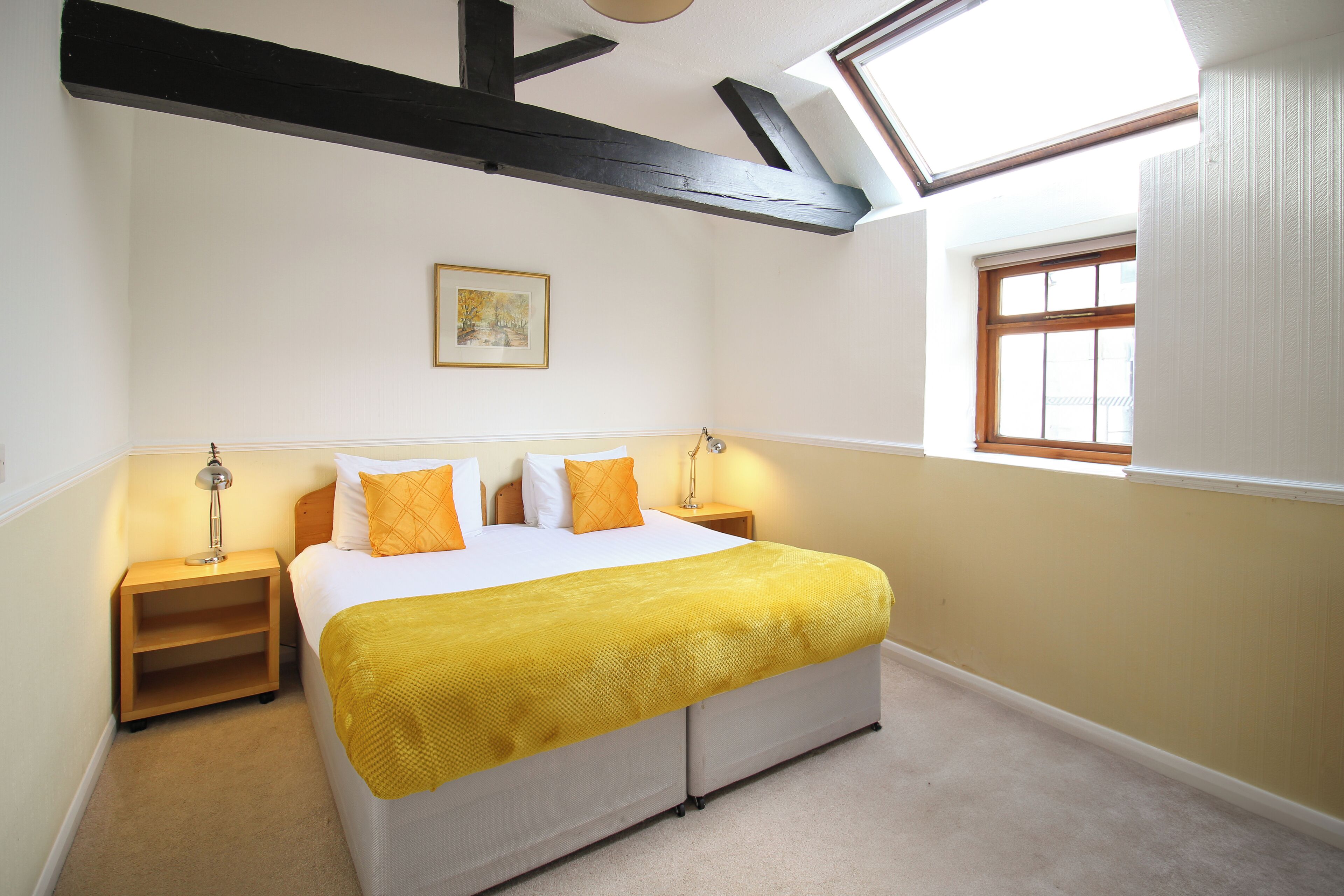 A bedroom with a bed, a nightstand, a lamp, a window, and a painting on the wall.