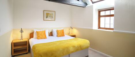 A bedroom with a bed, a nightstand, a lamp, a window, and a painting on the wall.