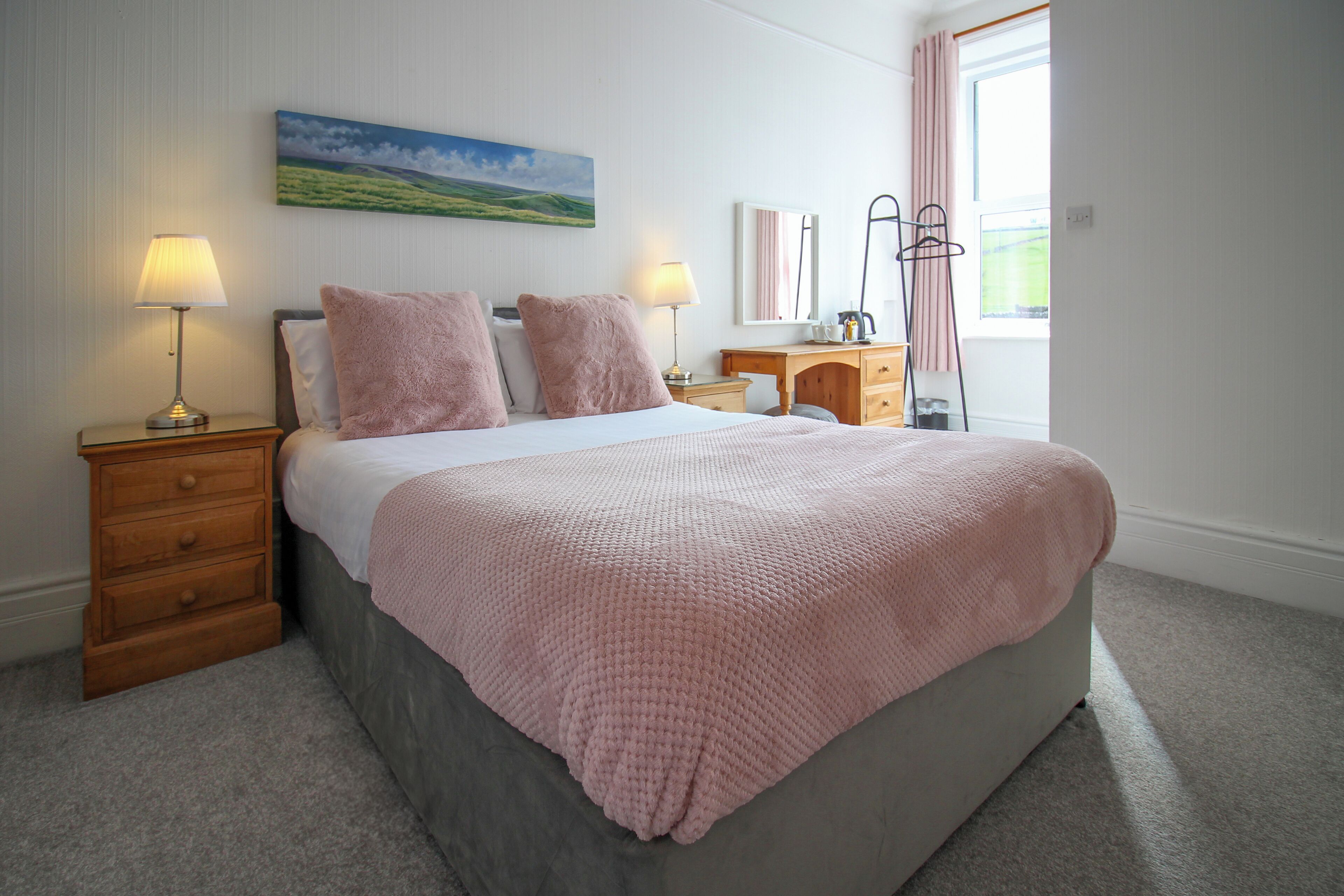 A bedroom with a bed, bedside tables, a desk, and a window with curtains.