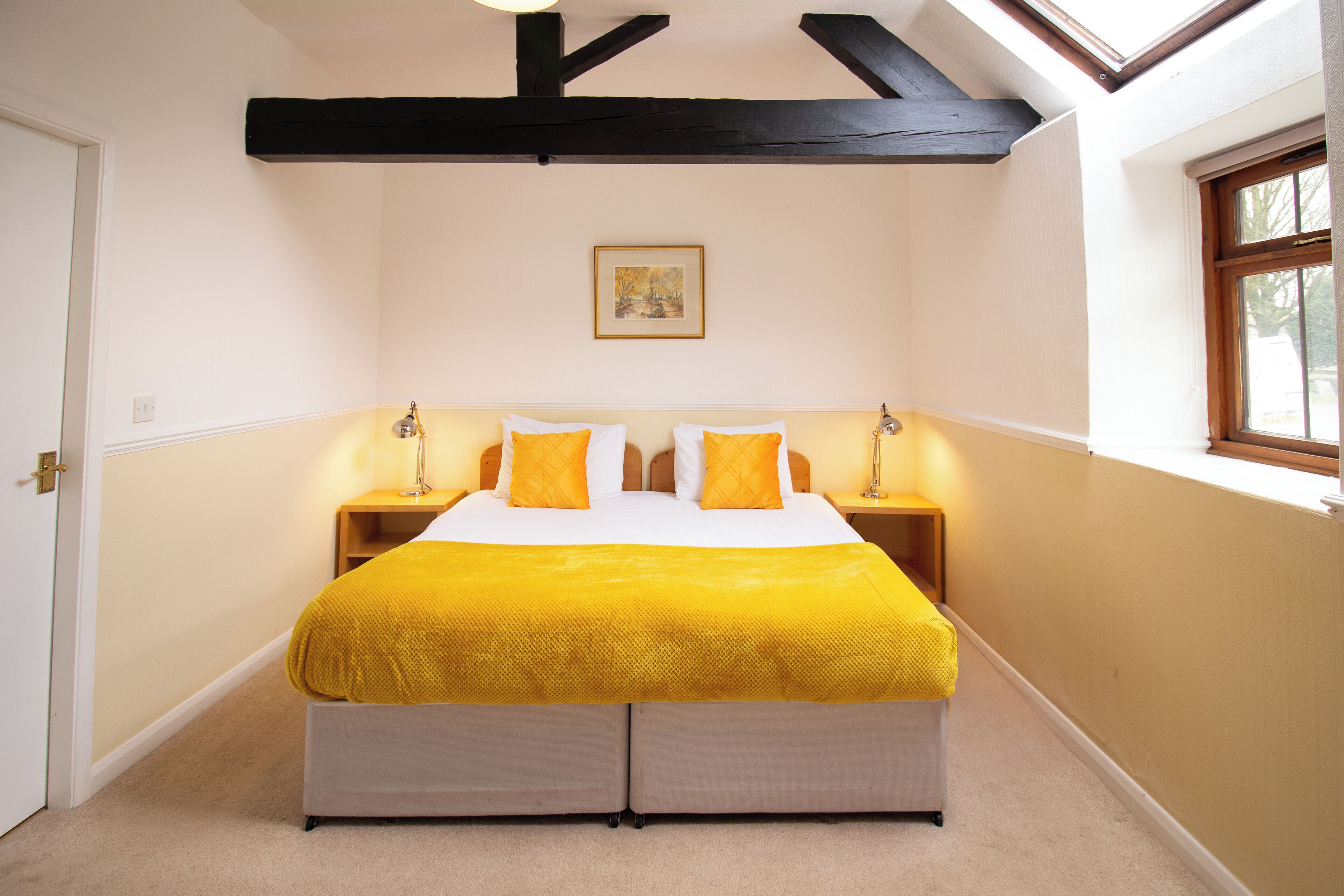 A bedroom with a bed, bedside lamps, a framed picture on the wall, and a window.