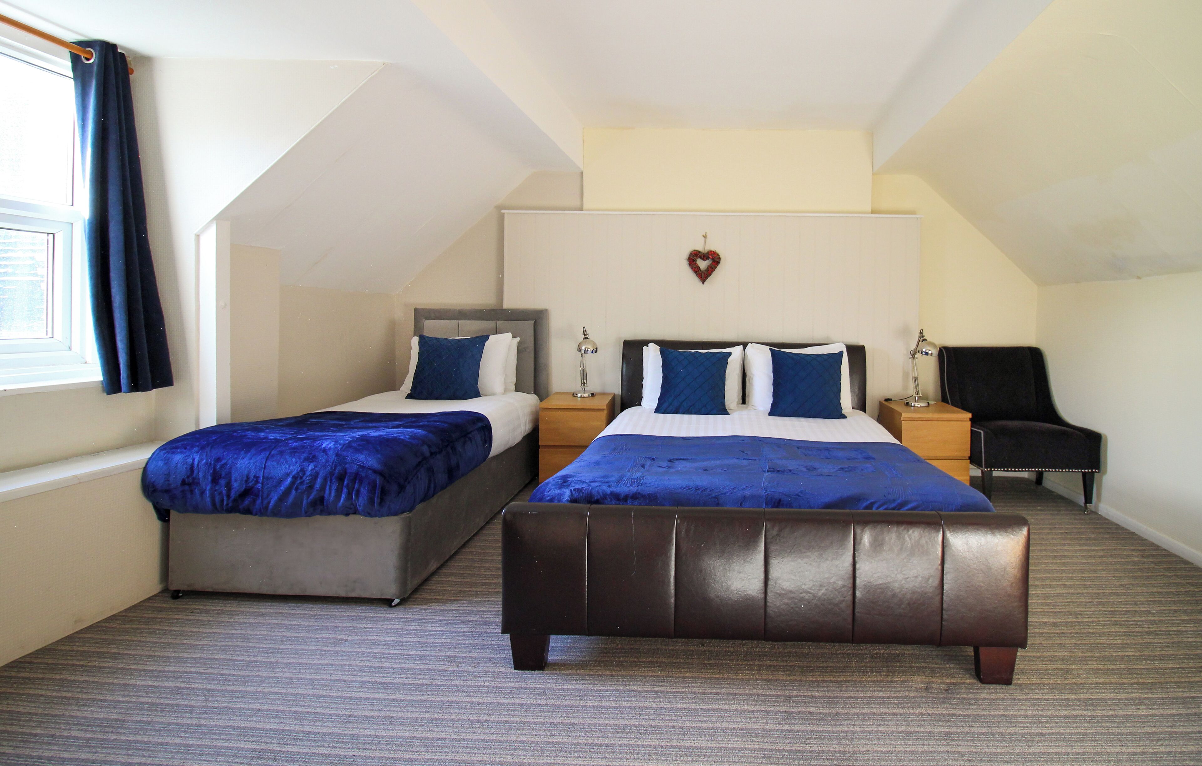 A room with two beds, a desk, a chair, and a heart-shaped decoration on the wall.