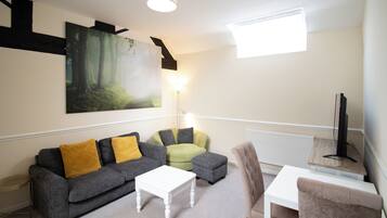 A modern living room with a grey sofa, a white coffee table, a green armchair, and a TV on a wooden stand.
