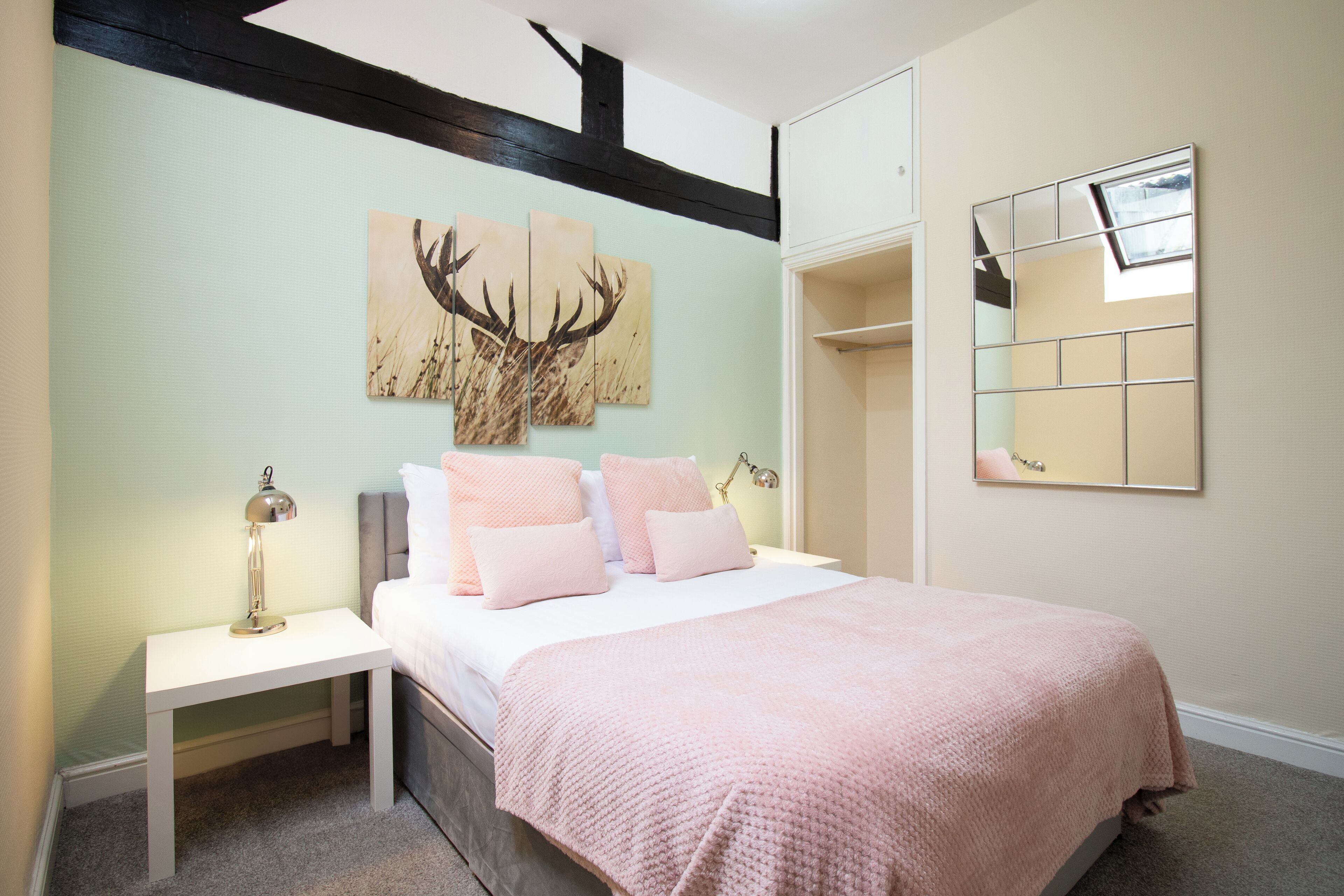 A bedroom with a bed, a nightstand, a mirror, and artwork on the wall.