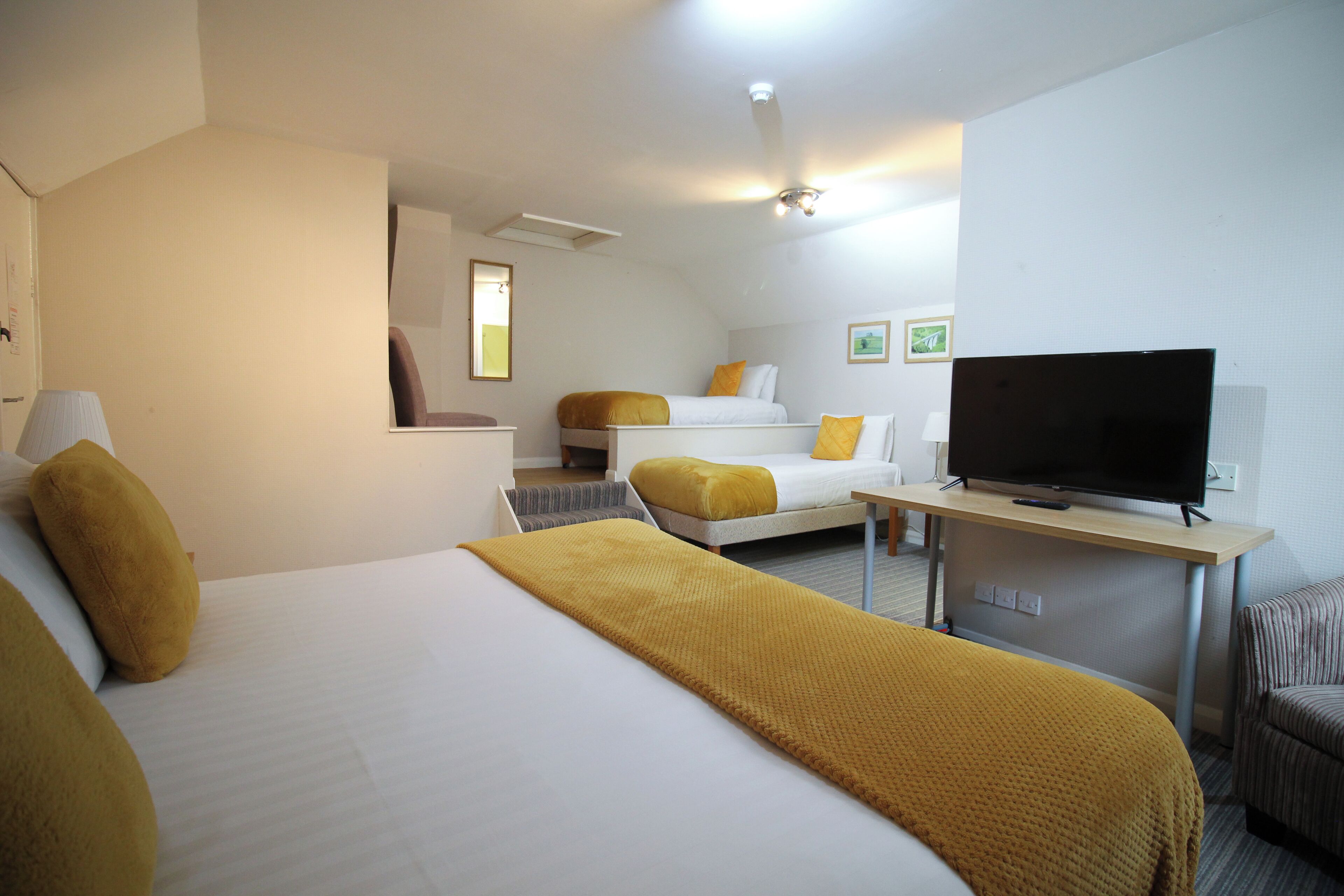 A hotel room with a large bed, a smaller bed, a TV, and a desk.