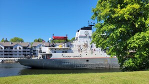 A large ship named 'MANITOWOC' docked near a waterfront with a grassy area in the foreground. - Riverside Motel and Marina Manistee (Manistee)