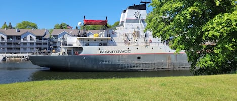 Un grand navire, baptisé « MANITOWOC », était amarré près d’une zone riveraine, avec une pelouse en premier plan.