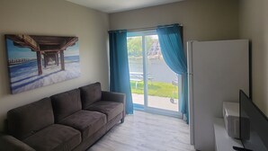 A modern living room with a sofa, a flat-screen TV, and a painting of a pier. - Riverside Motel and Marina Manistee (Manistee)