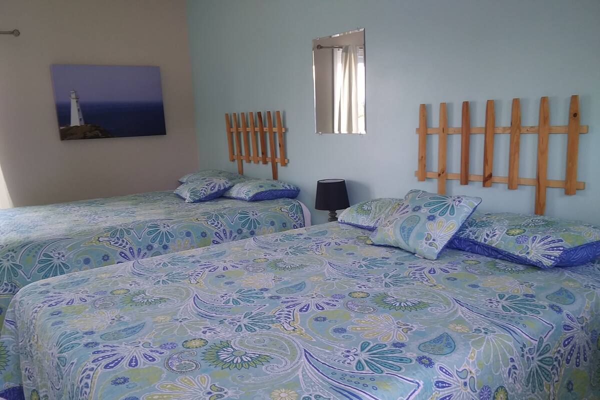 Una camera da letto con due letti, uno specchio, una lampada e un quadro raffigurante un faro.