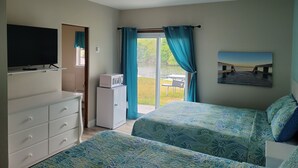 A bedroom with two beds, a TV, a microwave, and a view of a dock and water. - Riverside Motel and Marina Manistee (Manistee)