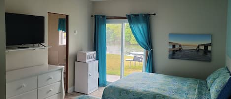 A bedroom with two beds, a TV, a microwave, and a view of a dock and water.