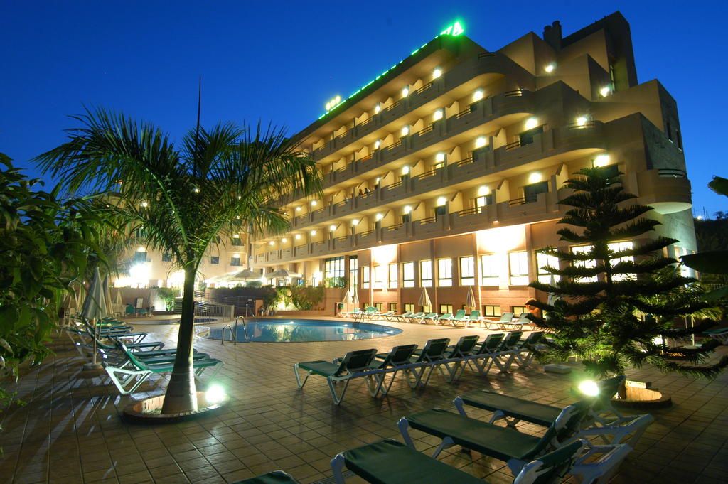 Un hotel con zona de piscina, varios balcones e iluminación exterior.