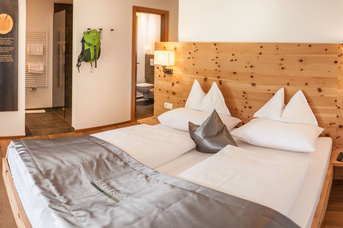 A modern hotel room with a large bed, a sofa, a small table, and a balcony with a view of the mountains.
