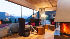 A modern lounge area with large windows, comfortable seating, a fireplace, and a view of mountains. - La Casies Mountain Living Hotel (Valle di Casies)