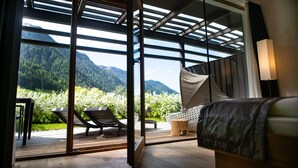 A bedroom with a large window, a bed, a chair, and a small table. - La Casies Mountain Living Hotel (Valle di Casies)