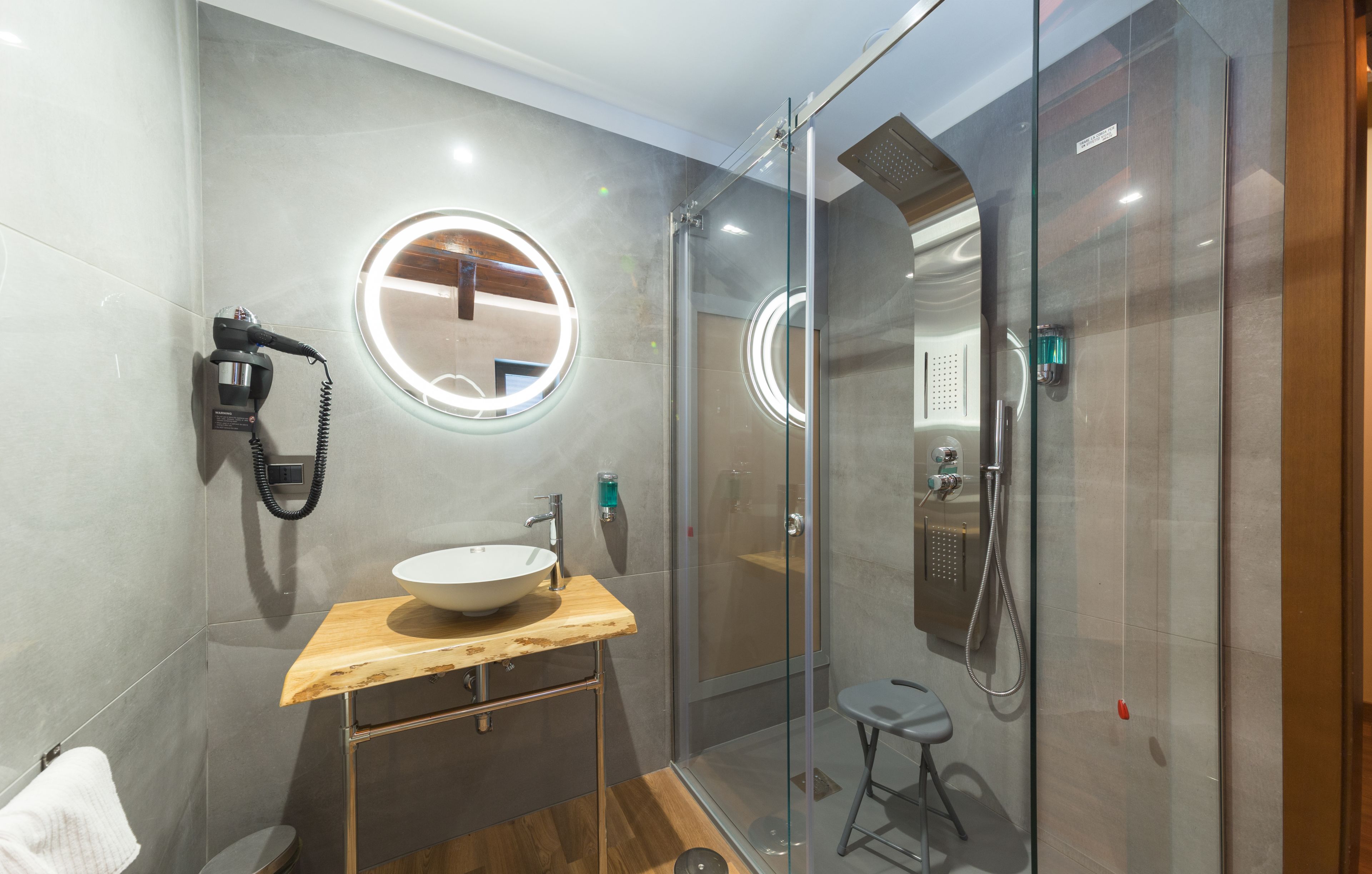Een moderne badkamer met een glazen douchecabine, een houten wastafelmeubel met een wastafel en een ronde spiegel.
