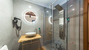 Een moderne badkamer met een glazen douchecabine, een houten wastafelmeubel met een wastafel en een ronde spiegel.