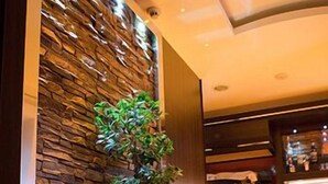 A modern reception area with a stone wall, a potted plant, and a bar counter. - Hotel Vogue (Giugliano in Campania)