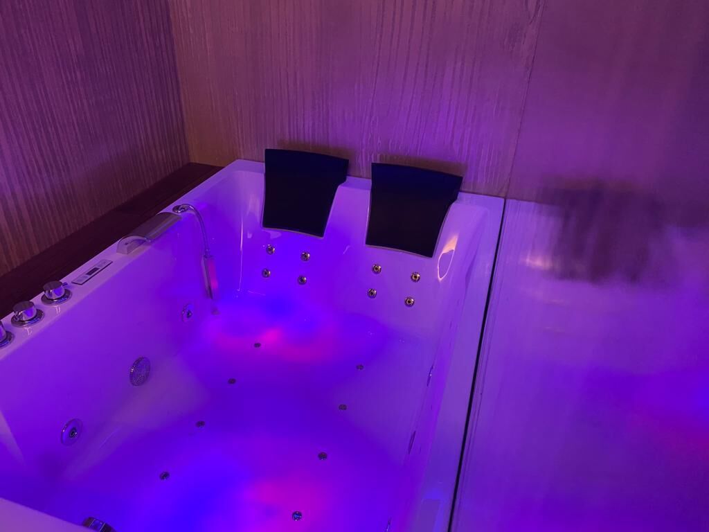 A bathtub with a wooden panel wall and a control panel on the left.