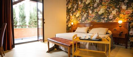 A bedroom with a bed, bench, bedside table, and a floral wallpaper.