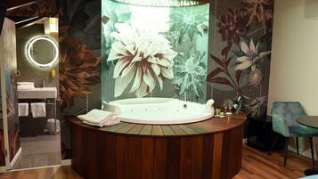 A modern bathroom with a round wooden vanity, a large mirror, a white bathtub, and a floral mural on the wall.