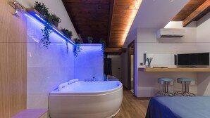 A modern bathroom with a freestanding bathtub, wooden ceiling beams, and a blue-lit wall. - Hotel Vogue (Giugliano in Campania)