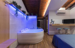 Un baño moderno con una bañera independiente, vigas de madera en el techo e iluminación azul en la pared.