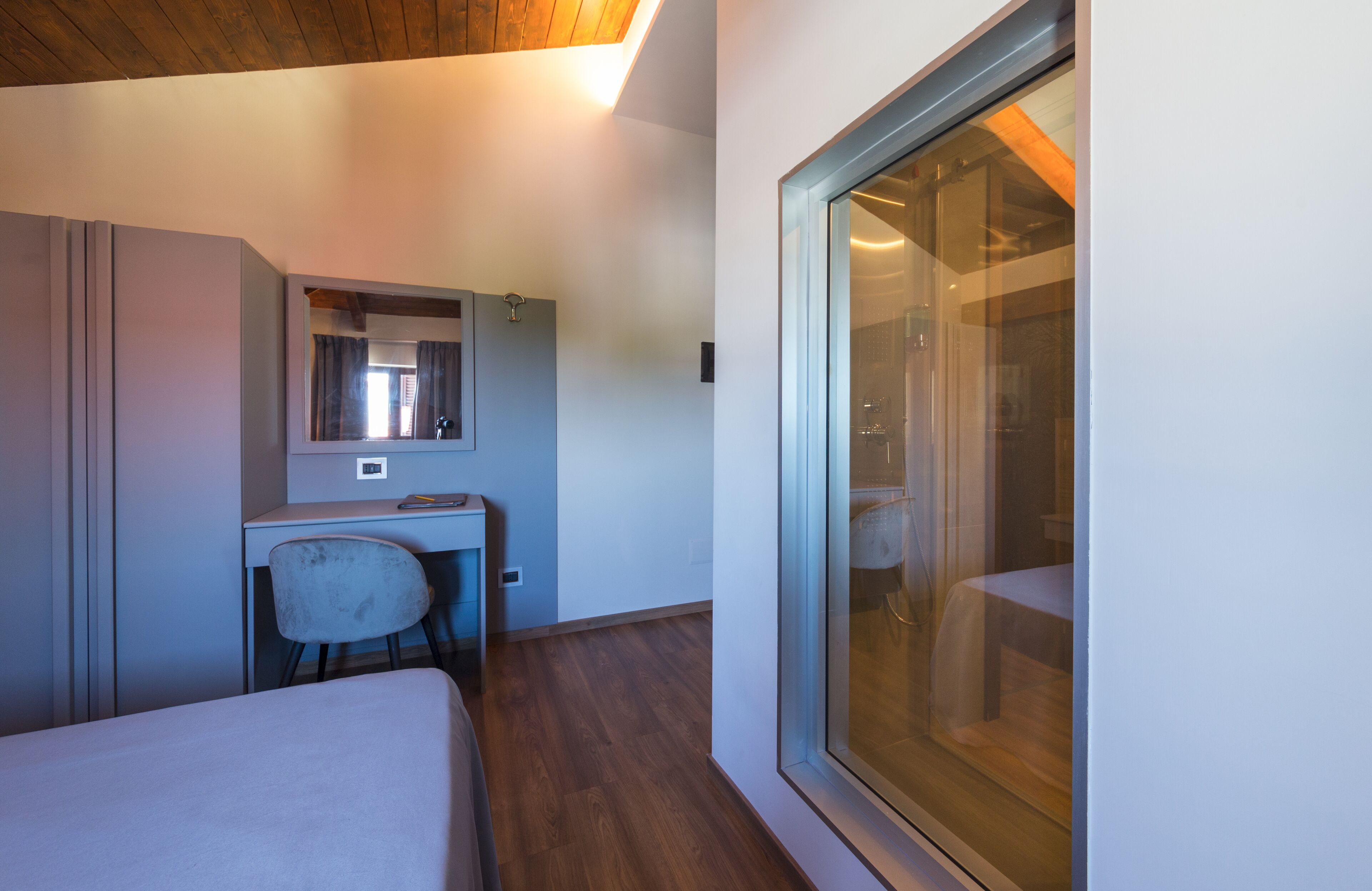A hotel room with a bed, a desk, a chair, a large window, and a mirror.