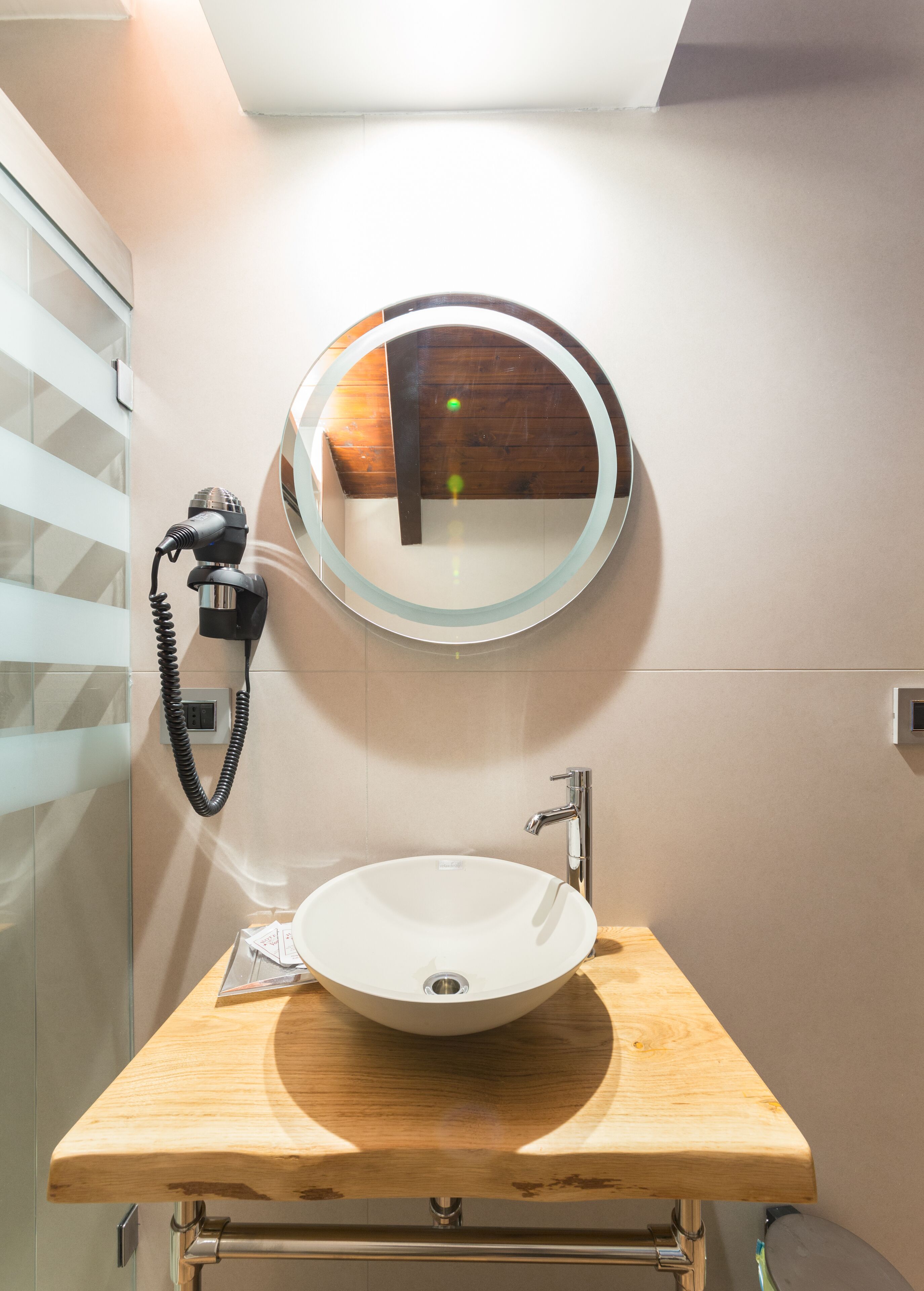 A bathroom with a round mirror, a white sink, and a hairdryer on a wall-mounted stand.