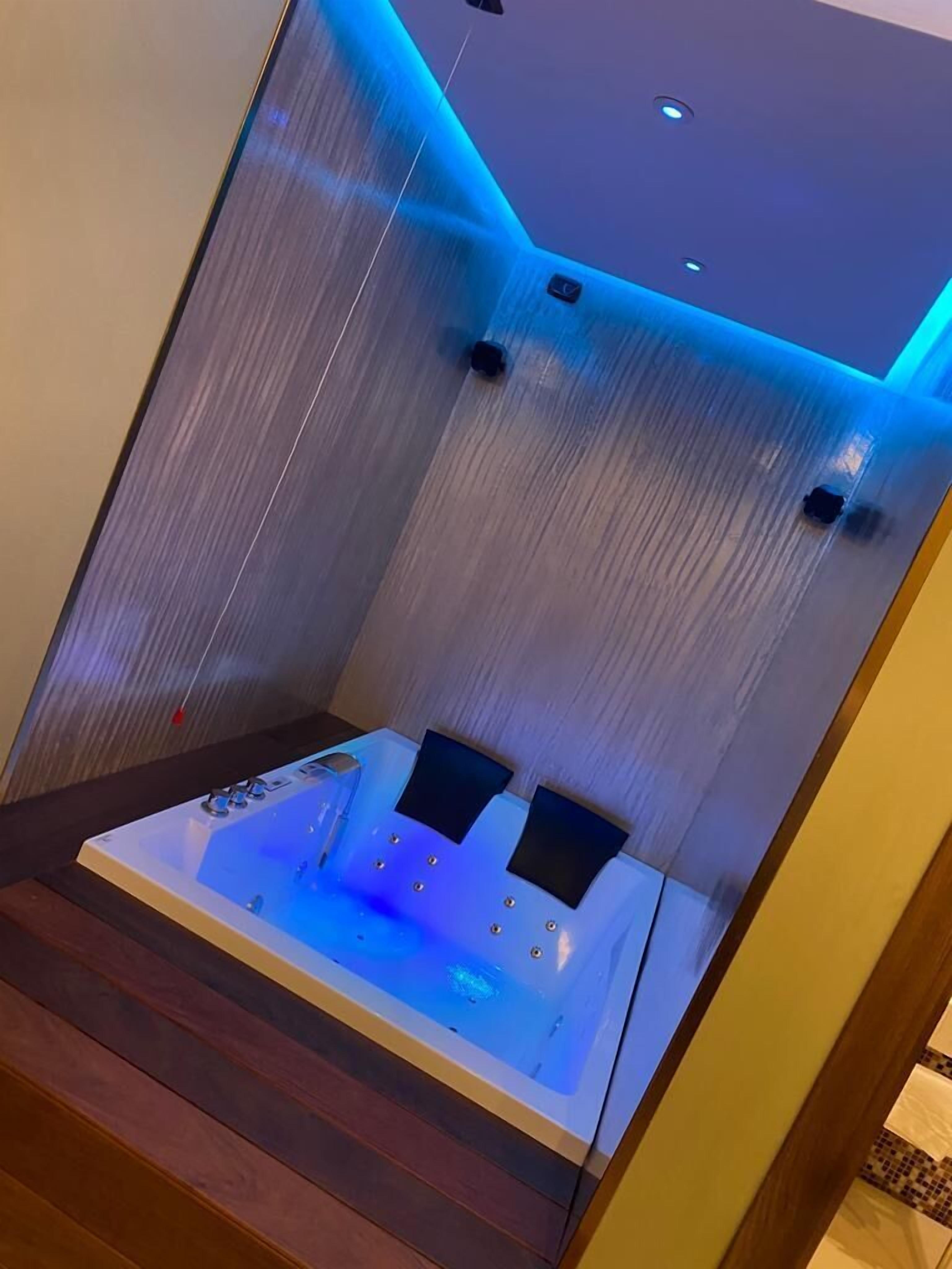 A modern spa room with a heated stone bath, ambient lighting, and a wooden floor.