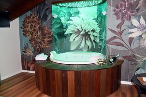 Un área de spa con un jacuzzi circular, suelo de madera y un gran mural floral en la pared.