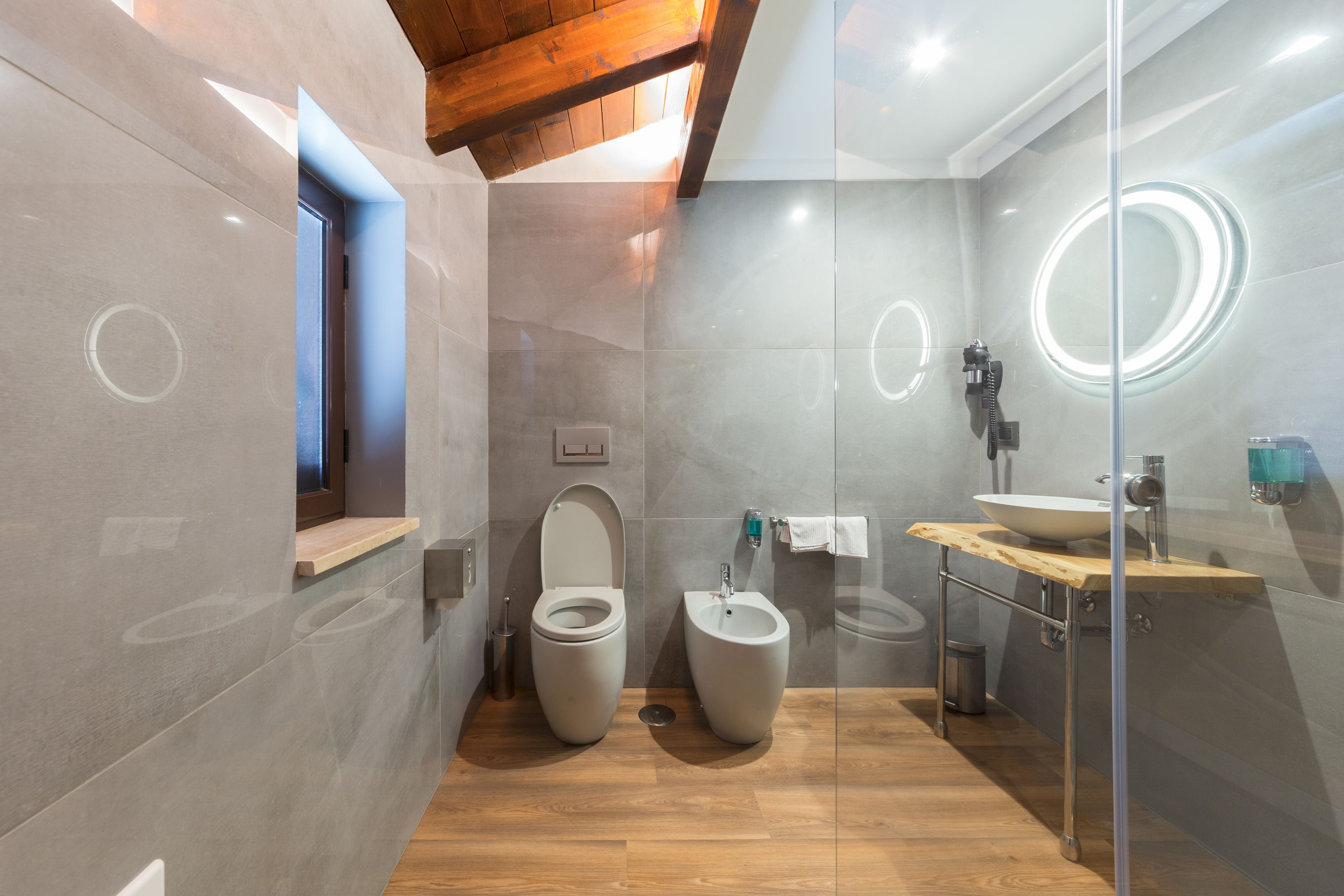 A modern bathroom with a wooden vanity, a bidet, and a glass-enclosed shower area.