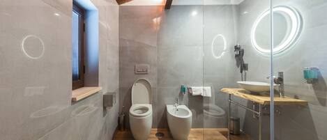 A modern bathroom with a wooden vanity, a bidet, and a glass-enclosed shower area.