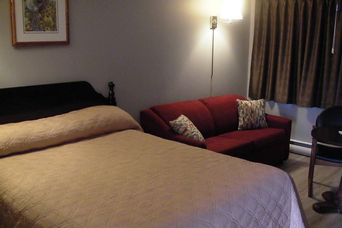 A hotel room with two beds, a red sofa, a chair, and a lamp.