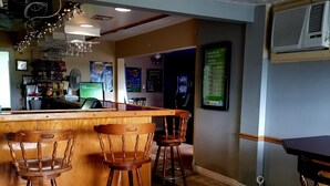 Zona de bar con sillas de madera, una barra y un aire acondicionado fijado a la pared.