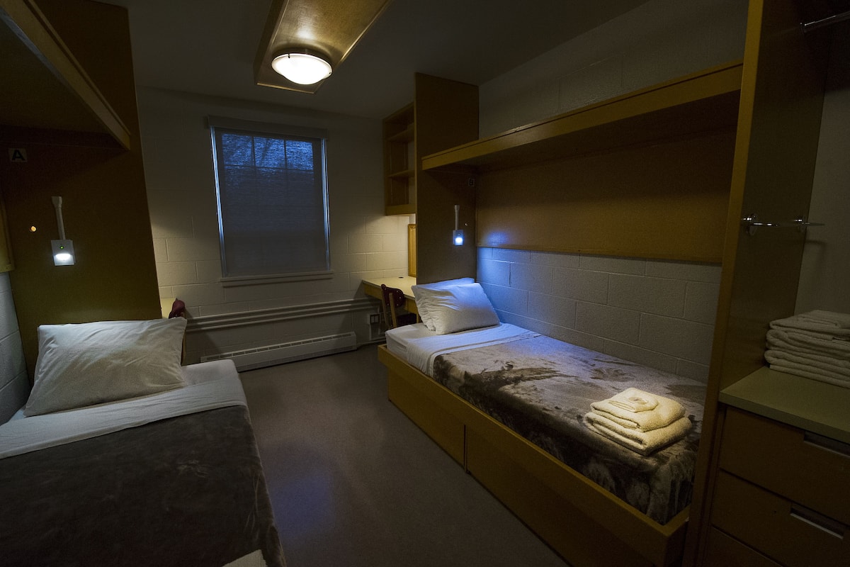 A dormitory room with bunk beds, a window, and a heater.