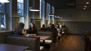 Un restaurante con cabinas y mesas, ventanas amplias e iluminación colgante.