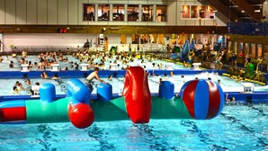 Una piscina interior con varias pistas, toboganes acuáticos inflables y un área para espectadores.