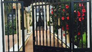 A black gate with vertical bars, leading to a pathway with a tiled floor. - Apartamentos Villa Rosalva (Puerto de la Cruz)