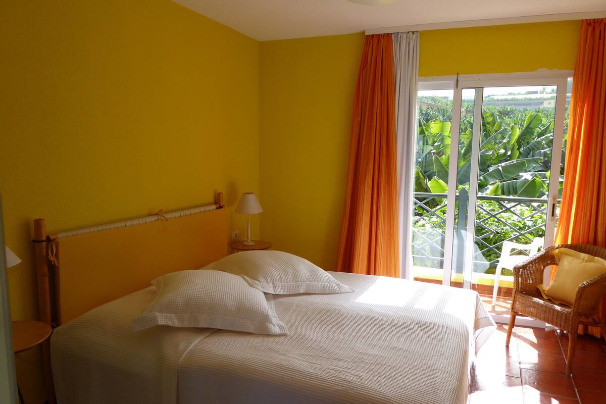 Ein Zimmer mit Bett, Stuhl und Blick auf Grünfläche.