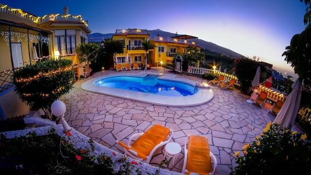 A circular pool with surrounding orange lounge chairs and a stone patio. - Apartamentos Villa Rosalva (Puerto de la Cruz)
